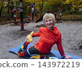 Mature woman practicing yoga and stretching outdoors in an autumn park. Active senior enjoying healthy aging, fitness, and vitality through outdoor workout and mindfulness. 143972219