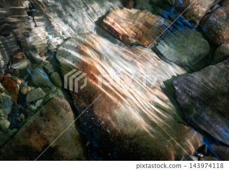 Sunlight refracts through clear water onto smooth stones in an abstract natural scene Sunlight refracts through clear water onto smooth stones in an abstract natural scene 143974118