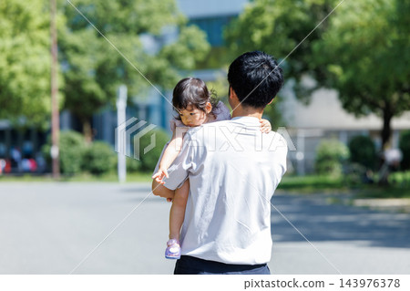 一位父親背對著鏡頭,抱著年幼的女兒在公園裡漫步。 一位父親背對著鏡頭,抱著年幼的女兒在公園裡漫步。 143976378