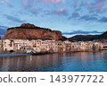 Sicilian seaside town dusk beneath dramatic rocky headland and pastel evening sky 143977722