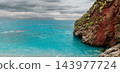 Turquoise coastal bay meets a rugged red rock headland beneath a dramatic cloudy sky 143977724