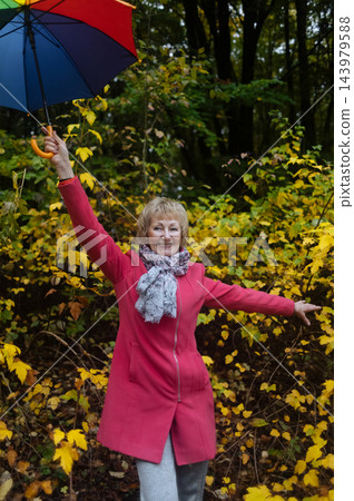 Active senior woman holding colorful umbrella smiling and enjoying autumn wellness in park. Mature female lifestyle and healthy aging Active senior woman holding colorful umbrella smiling and enjoying autumn wellness in park. Mature female lifestyle and healthy aging 143979588
