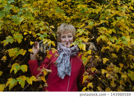 Happy senior woman in pink coat smiling outdoors in autumn park. Active elderly lifestyle, healthy aging and seasonal wellness concepts. 143980589