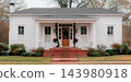 JEFFERSON, TEXAS: A clean, symmetrical white historic home with wide red brick steps, a natural wood front door, and subtle Christmas garland and poinsettia decorations. 143980918