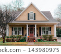 JEFFERSON, TEXAS: A cozy beige craftsman house with a red front door, white rocking chairs on the front porch, brick foundation, and holiday decorations. 143980975