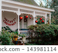 JEFFERSON, TEXAS: A white historic home's front porch decorated for the holidays with large red hanging ornament balls, string lights, and festive holiday decor. 143981114