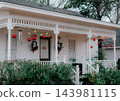 JEFFERSON, TEXAS: A white historic home's front porch decorated for the holidays with large red hanging ornament balls, string lights, and festive holiday decor. 143981115