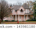 JEFFERSON, TEXAS: A stunning two-story pink Victorian home featuring a corner turret tower, wraparound front porch, and historic architectural details surrounded by fall foliage. 143981180