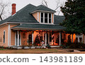 JEFFERSON, TEXAS: A warm light-orange historic house decorated for Christmas at dusk, featuring illuminated string lights, festive garland, and Christmas trees on the porch. 143981189