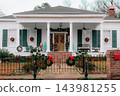 JEFFERSON, TEXAS: A classic white historic home adorned for Christmas with green shutters, red bows, wreaths, a wrought-iron fence, and holiday decorations on the front porch. 143981255