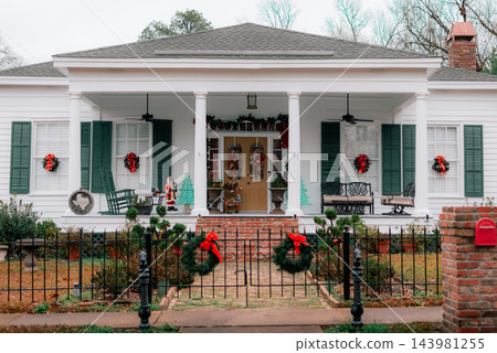 JEFFERSON, TEXAS: A classic white historic home adorned for Christmas with green shutters, red bows, wreaths, a wrought-iron fence, and holiday decorations on the front porch. JEFFERSON, TEXAS: A classic white historic home adorned for Christmas with green shutters, red bows, wreaths, a wrought-iron fence, and holiday decorations on the front porch. 143981255