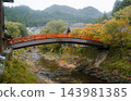 UDA, NARA, JAPAN: A traditional red vermilion arched wooden bridge spanning across a shallow rocky river toward Murou-ji temple amidst autumn trees and misty forested mountains. 143981385