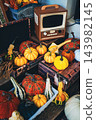 vintage television resting on patterned suitcase surrounded by autumn pumpkins, retro wooden radio near glowing lamp featuring seasonal knitted squash decoration 143982145