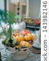 striped orange pumpkins and green gourd in white colander on lace table, cozy autumn harvest decoration featuring seasonal squash near vintage candlestick 143982146