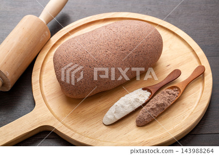 raw sorghum flour dough for making homemade noodles, placed on a wooden peel with rolling pin and wooden spoons of flour. raw sorghum flour dough for making homemade noodles, placed on a wooden peel with rolling pin and wooden spoons of flour. 143988264