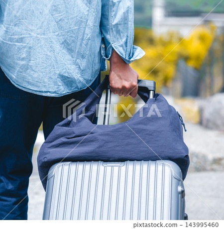 一個男人背對著鏡頭，拉著行李箱準備出發旅行。 143995460