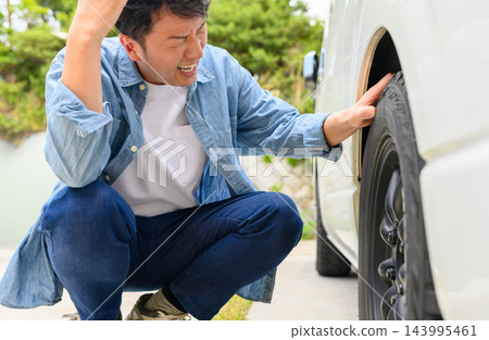 一個男人因為汽車輪胎癟了而束手無策。 143995461