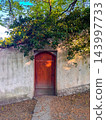 Arched wooden door is set into stone wall, heavily overgrown with green vines 143997733