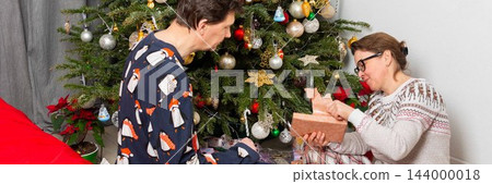 On Christmas Day, a 52-year-old couple spends time together near a decorated tree. They exchange gifts and celebrate the holiday in their cozy home setting filled with decorations On Christmas Day, a 52-year-old couple spends time together near a decorated tree. They exchange gifts and celebrate the holiday in their cozy home setting filled with decorations 144000018