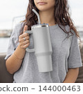Blank light gray 40oz tumbler mockup, young woman outdoors close up. Lifestyle coastal scene 144000463