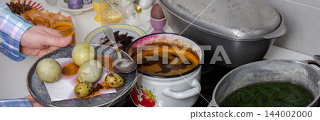 Hands prepare eggs for Easter by dyeing them with turmeric and dried Sudanese rose hibiscus in pots on a kitchen stove, banner 144002000