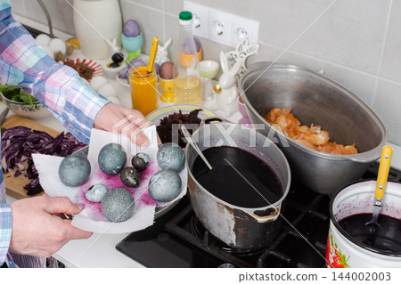Hands dye eggs with red cabbage in pots on a kitchen stove, then place the eggs on a plate during Easter preparations at home Hands dye eggs with red cabbage in pots on a kitchen stove, then place the eggs on a plate during Easter preparations at home 144002003