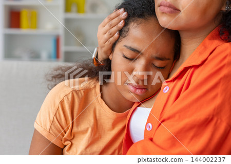 Black daughter is resting her head against her mothers chest at home Black daughter is resting her head against her mothers chest at home 144002237