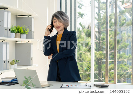 Businesswoman Standing and Talking on Smartphone in Office Businesswoman Standing and Talking on Smartphone in Office 144005192