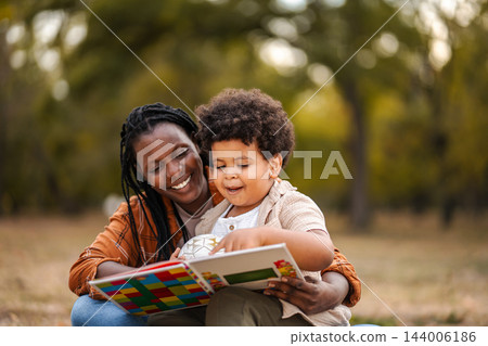 Mother and son reading book outdoors in park Mother and son reading book outdoors in park 144006186