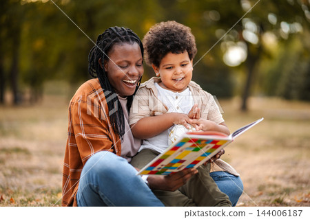 Mother son reading storybook enjoying family time outdoors Mother son reading storybook enjoying family time outdoors 144006187