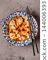 Wontons are placed in a bowl with spicy sauce. 144006393
