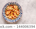 Wontons are placed in a bowl with spicy sauce. 144006394