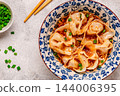 Wontons are placed in a bowl with spicy sauce. 144006395