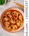 Wontons are placed in a bowl with spicy sauce. 144006397