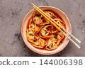 Wontons are placed in a bowl with spicy sauce. 144006398