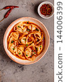 Wontons are placed in a bowl with spicy sauce. 144006399