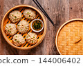 Steam basket with dumplings served with dipping sauce on a wooden table 144006402