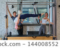Personal trainer coaching two clients on Cadillac equipment - wide view 144008552