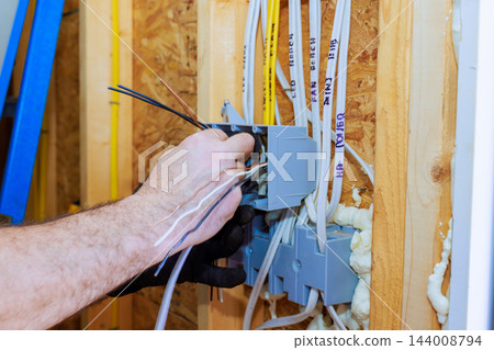 Hand working with multiple electrical wires inside gray junction box on wooden wall framing 144008794