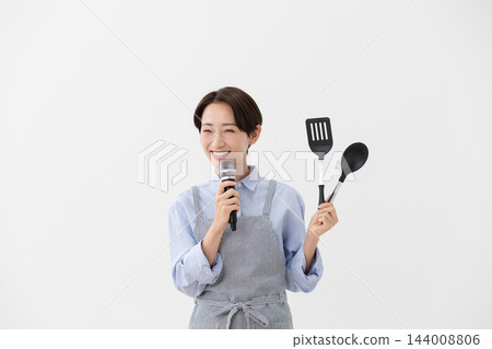一張烹飪圖片,圖中一位女士一手拿著麥克風,一手拿著鍋鏟。 一張烹飪圖片,圖中一位女士一手拿著麥克風,一手拿著鍋鏟。 144008806
