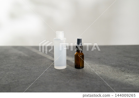灰色桌子上放著一個白色瓶子和一個棕色噴霧瓶。 灰色桌子上放著一個白色瓶子和一個棕色噴霧瓶。 144009265