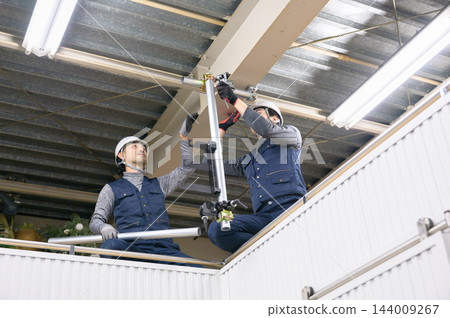 兩名男工人在室內建築工地一起組裝鷹架管。 兩名男工人在室內建築工地一起組裝鷹架管。 144009267