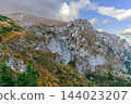 Rugged rocky mountain ridge rises above autumn vegetation beneath a dramatic cloud-filled sky 144023207