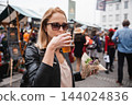 Beautiful young woman holding delicious organic salmon vegetarian burger and drinking homebrewed IPA beer on open air beer an burger urban street food festival in Ljubljana, Slovenia 144024836