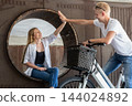 Happy young couple giving high five while meeting outdoors with e-bike. Friends greeting each other with high five in modern urban setting. 144024892