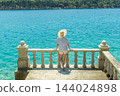Rear view of woman wearing straw summer hat ,leaning against elegant old stone fence of coastal villa, relaxing while looking at blue Adriatic sea, on Losinj island Croatia. 144024898