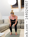 Beautiful blonde woman doing home workout indoors. Woman practice yoga at home. Fit girl using workout tutorials for healthy active lifestyle. Woman using quarantine for home workouts. Stretching 144024907