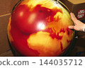 A photograph showing a hand resting on a globe dyed red and orange. 144035712