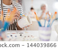 Hands of female artisan painting mug in pottery workshop 144039866