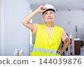 Portrait of positive builder woman in protective helmet and yellow vest in renovated room 144039876